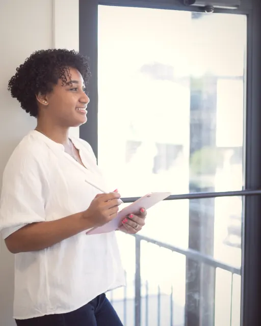 A woman standing at a window with a tablet, talking through a plan
