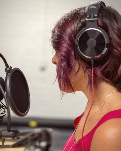 A woman recording a piece to camera at a studio microphone